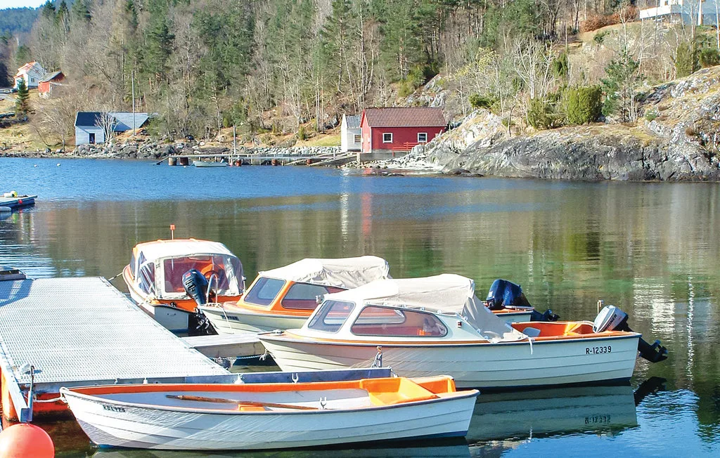 Boats are moored beside a dock on a calm lake, with wooded hills beyond.
