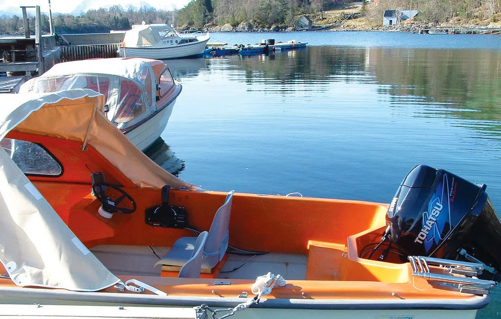 A small motorboat with orange seating is moored on a calm harbor.