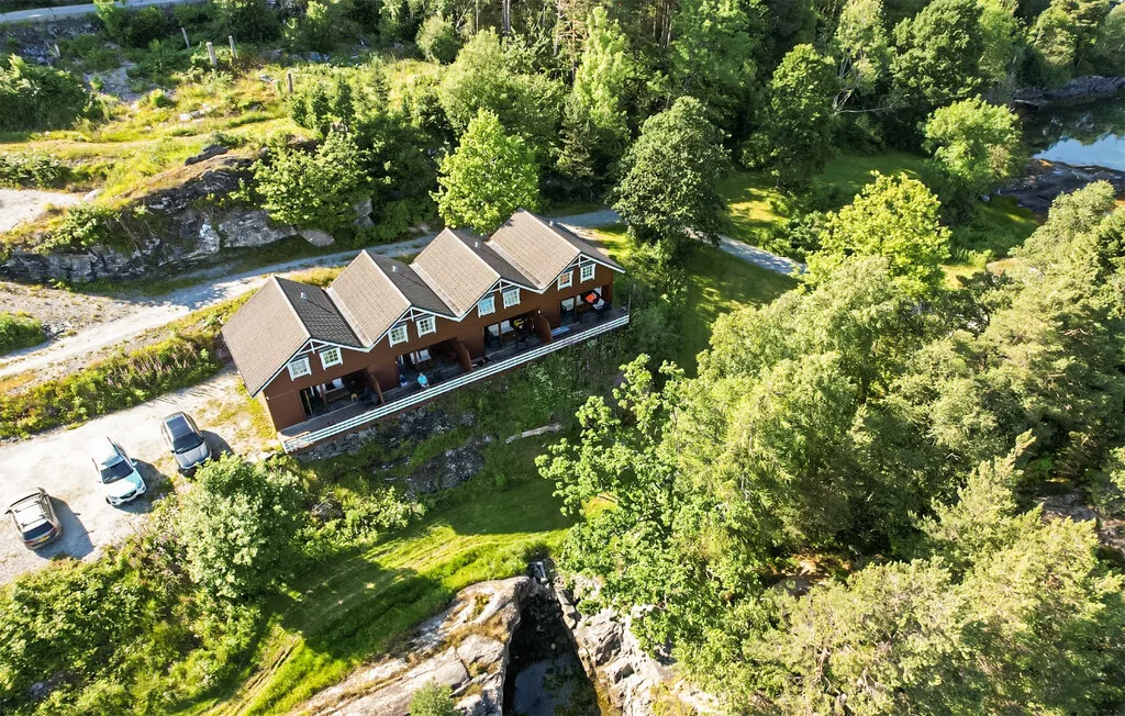 Aerial view of several connected cabins beside a wooded rocky landscape.