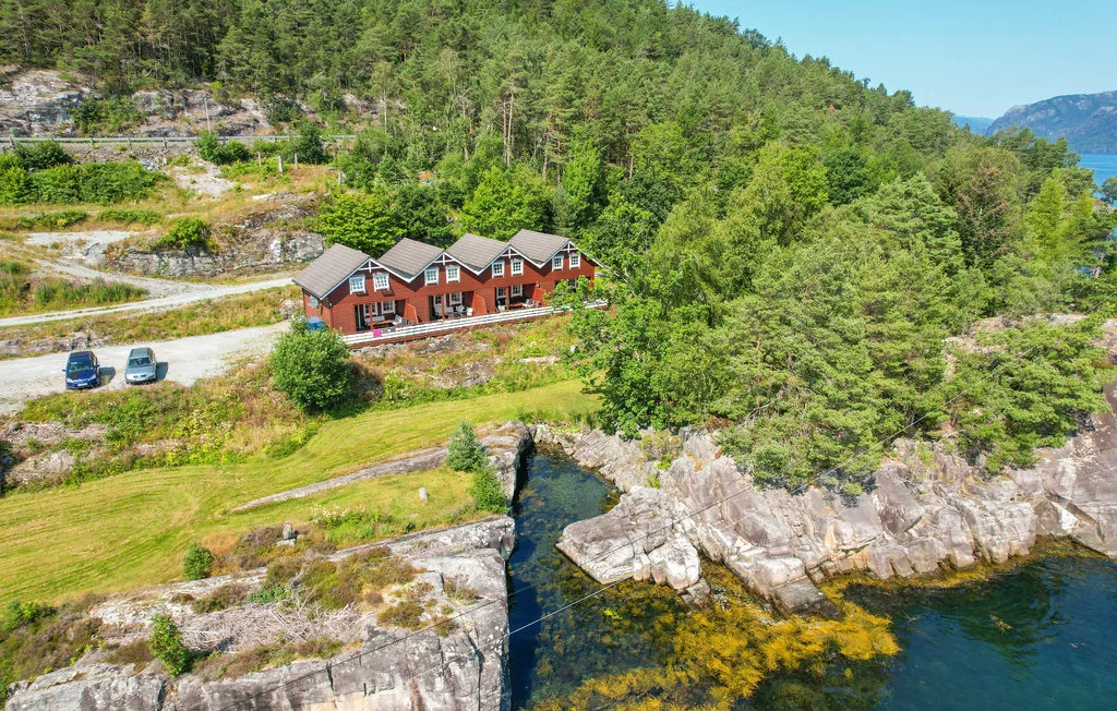A group of red cabins sits among wooded hills beside a rocky shoreline.