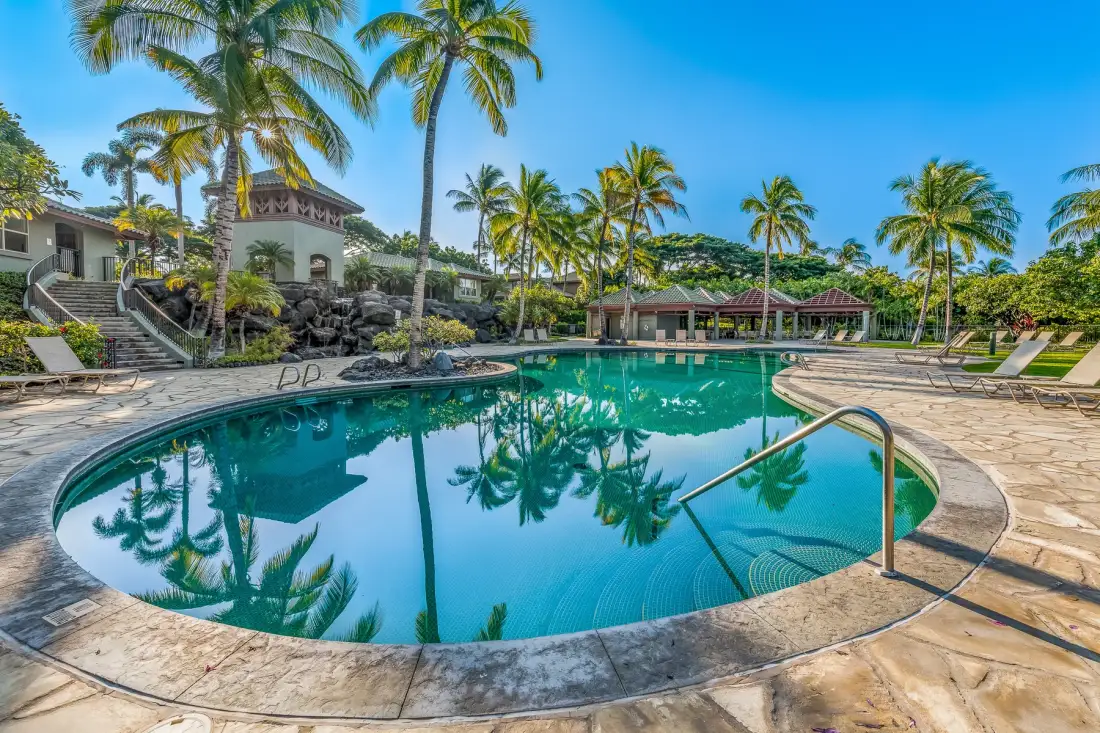 Una piscina está rodeada de palmeras y asientos al aire libre.