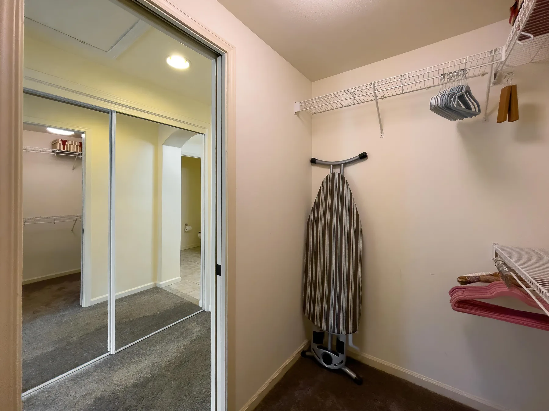 Un vestidor con estantes de alambre, prendas colgadas y un espejo de cuerpo entero.