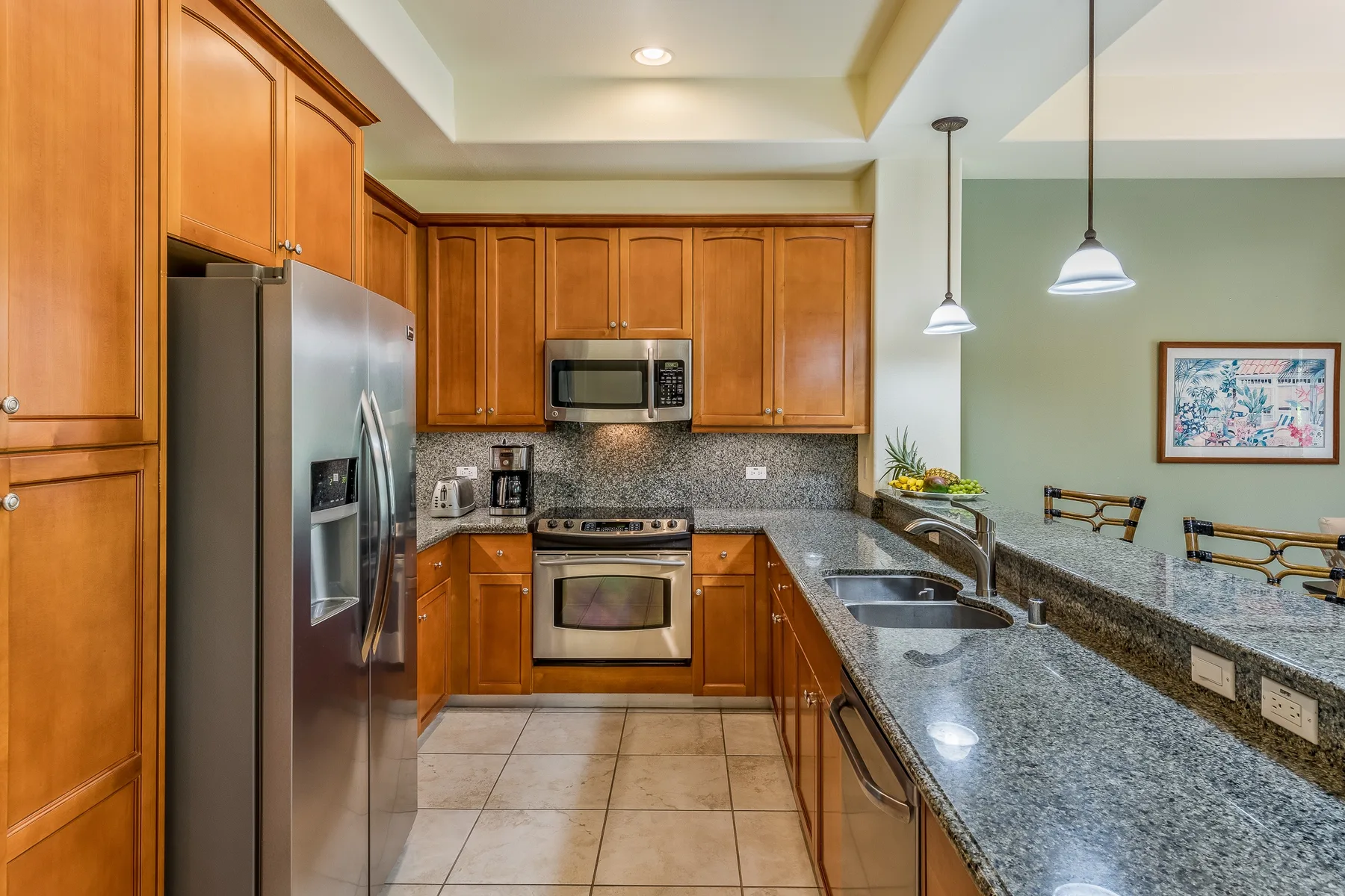 A kitchen with wooden cabinets, stainless steel appliances, and a long stone countertop.
