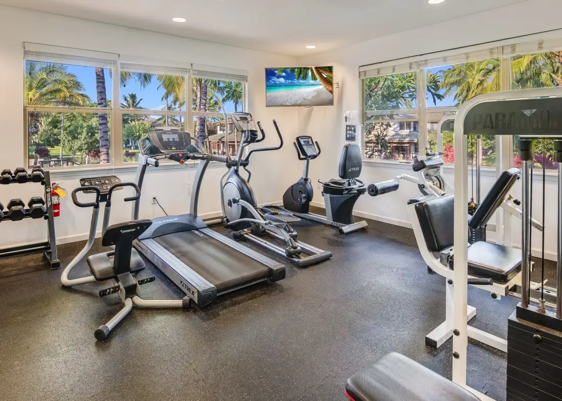 Un gimnasio con cintas de correr y máquinas de ejercicio junto a grandes ventanas.