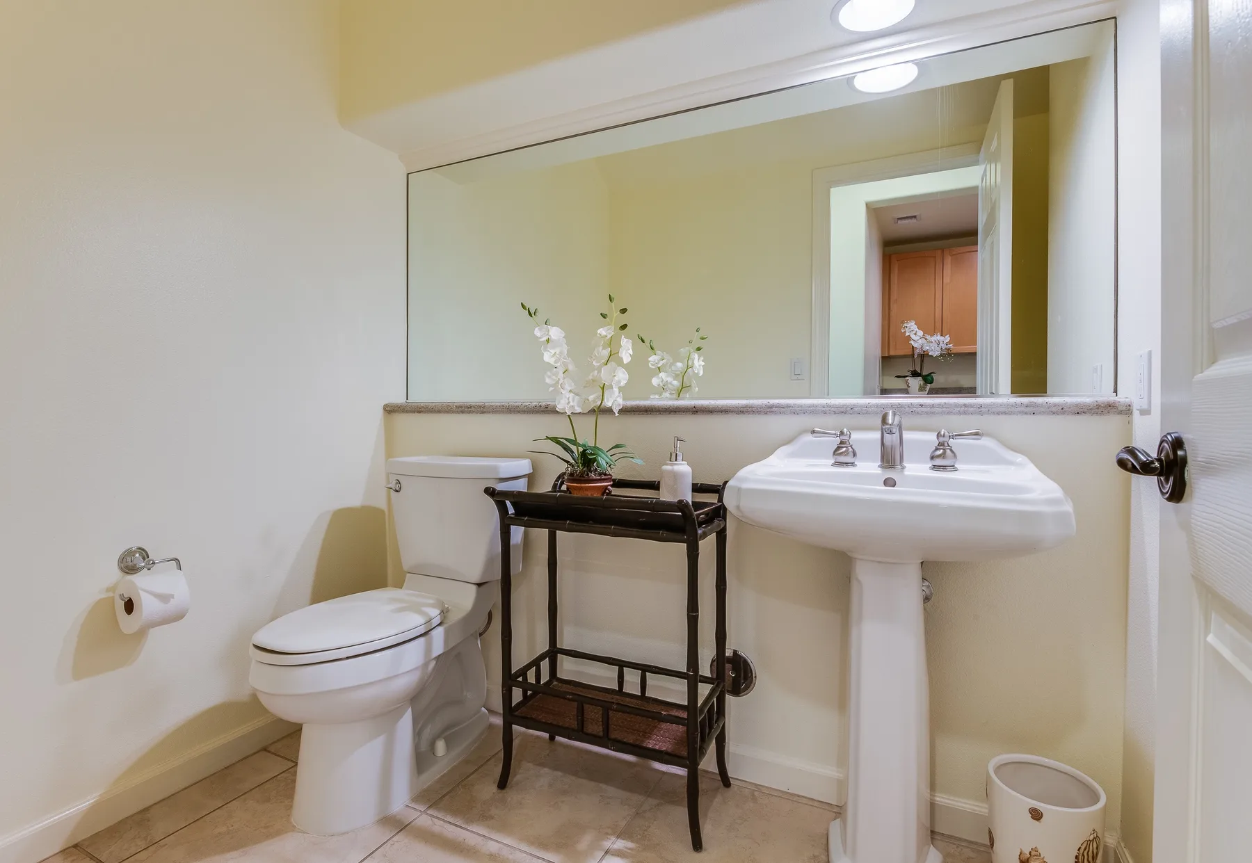 Un baño con inodoro, lavabo de pedestal y un espejo grande.