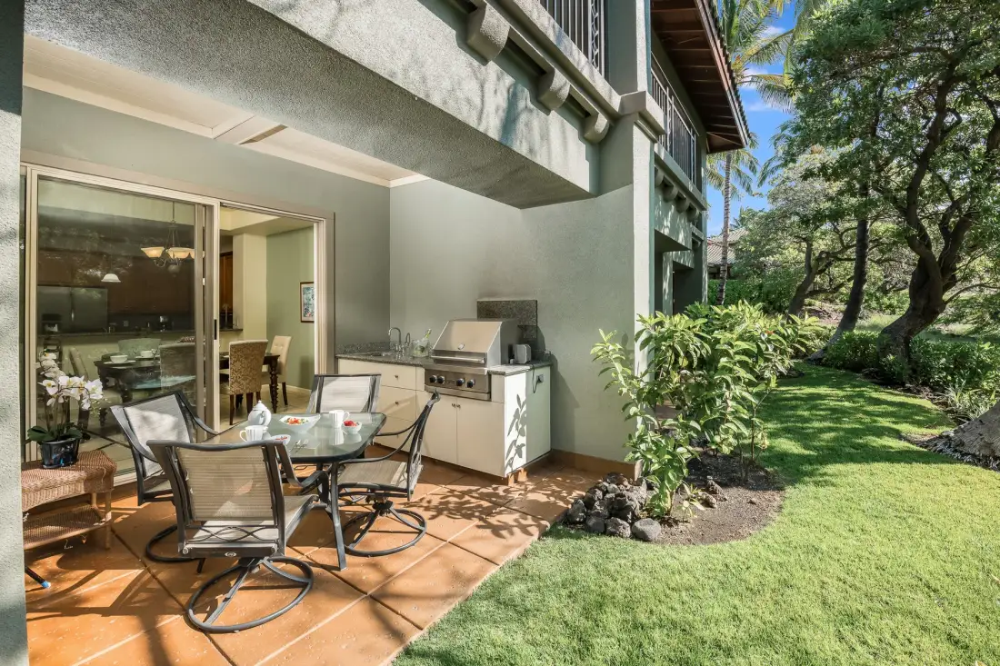 Una zona de estar en el patio con mesa y mostrador exterior junto a un césped verde.