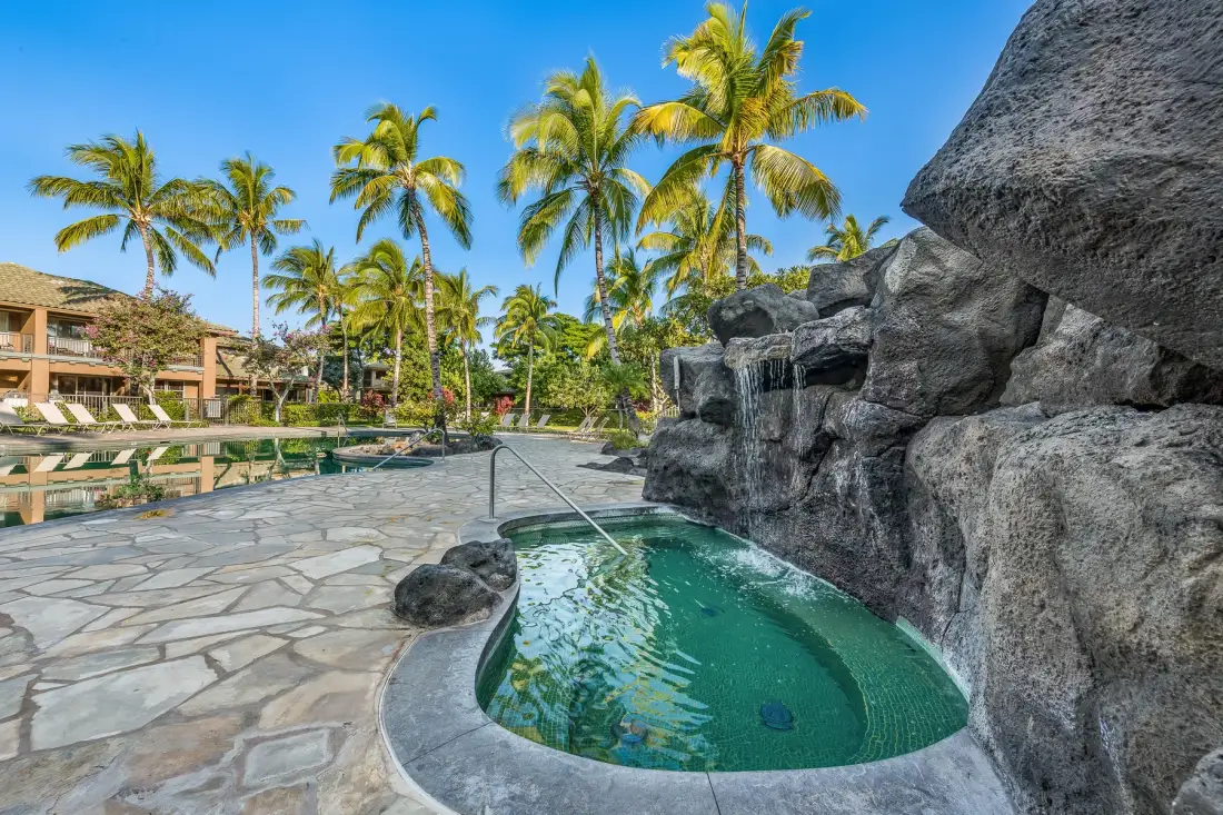 Una pequeña piscina está junto a una cascada rocosa en un patio tropical.