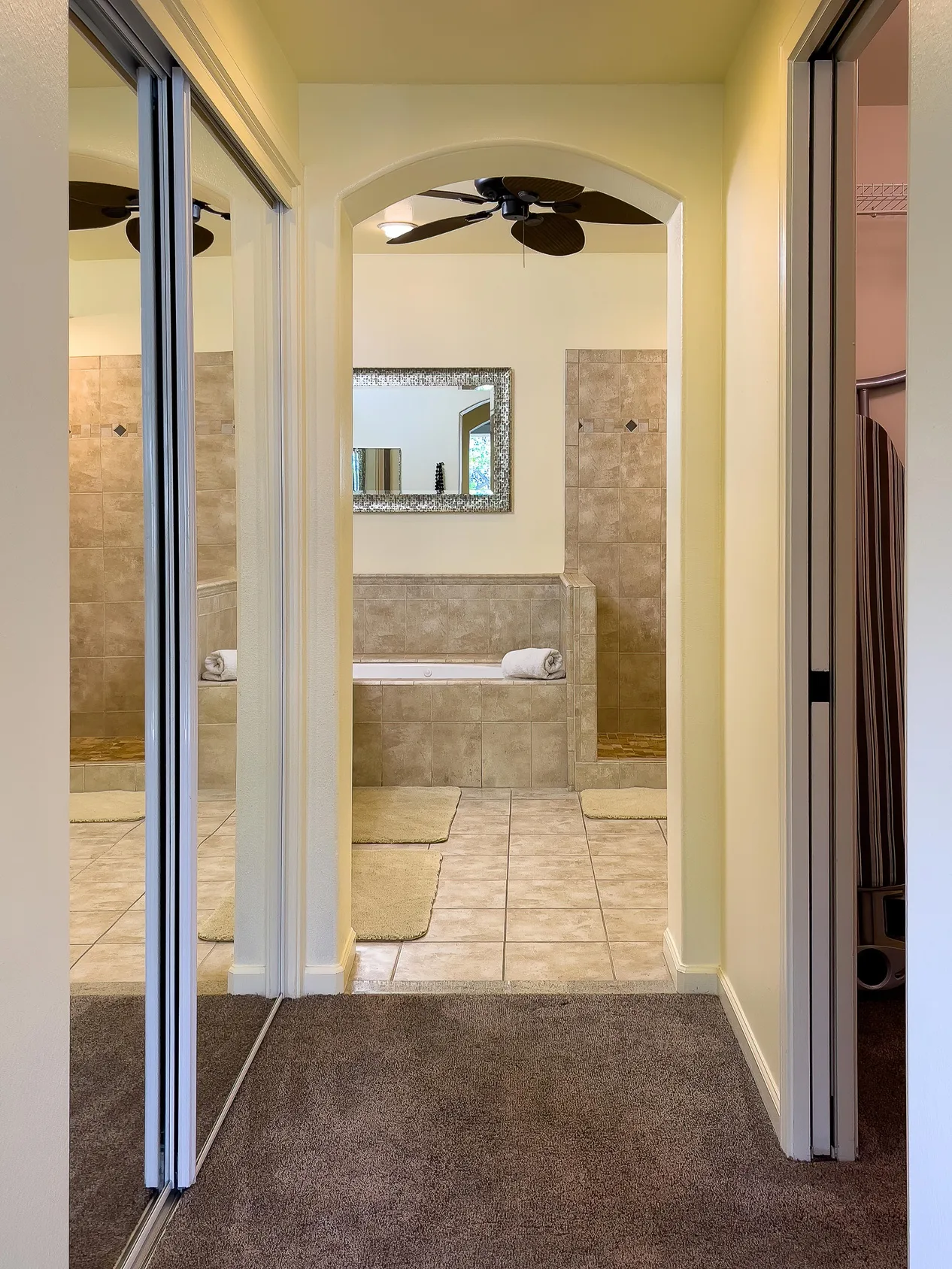 Un baño con azulejos, una bañera y un espejo bajo un ventilador de techo.