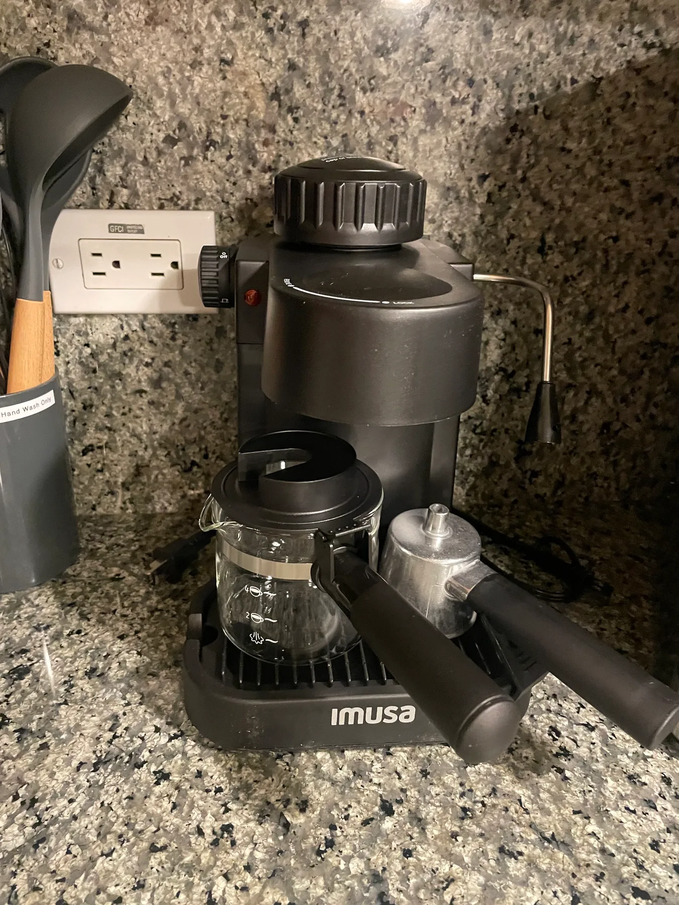 Una cafetera está sobre una encimera de cocina junto a un recipiente para utensilios.