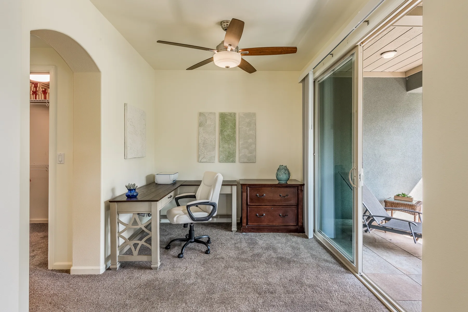 Un estudio luminoso con escritorio, silla y puertas corredizas de vidrio que dan a un patio.
