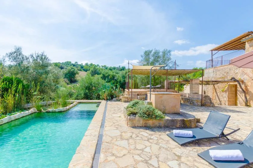 An outdoor pool beside a stone patio with a reclining lounger.