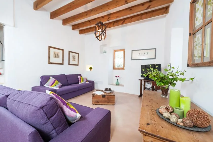 A living room with purple seating, a wooden coffee table, and exposed ceiling beams.