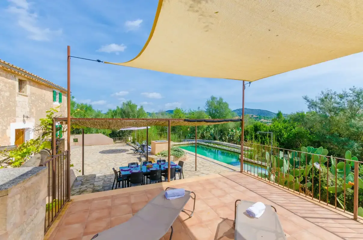 A shaded outdoor terrace overlooks a swimming pool and green landscape.