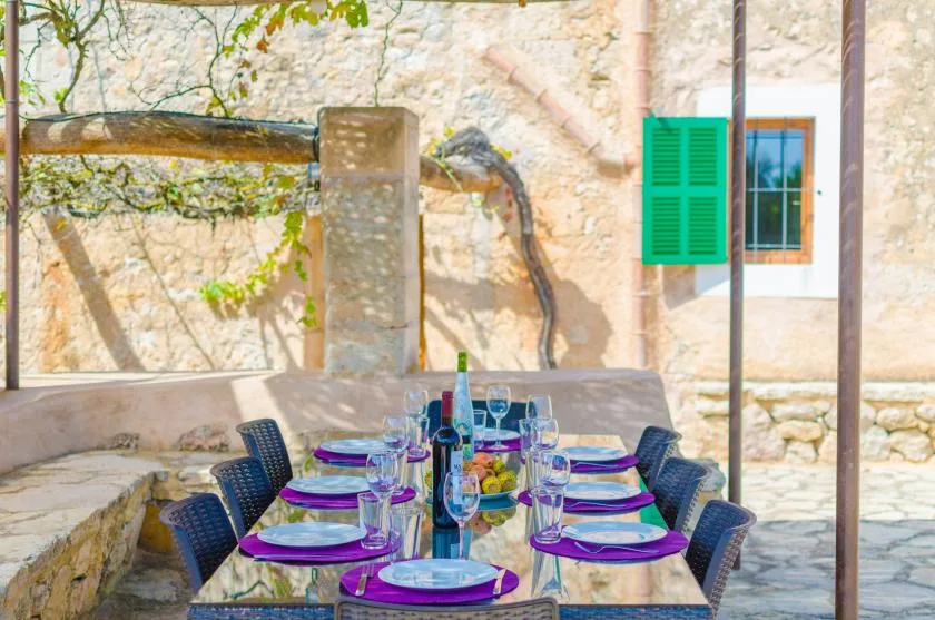 An outdoor dining area with a set table beneath a stone wall and window.