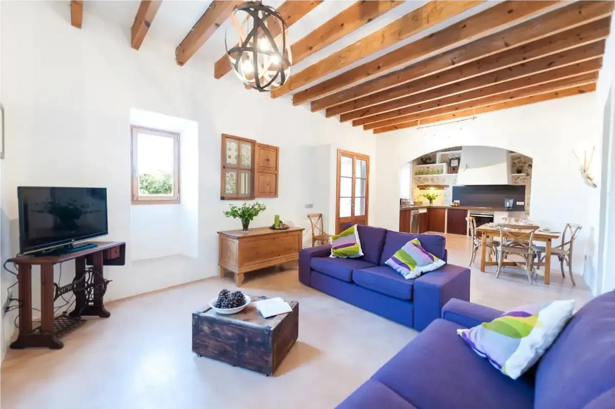 A bright living room with blue seating and exposed wooden ceiling beams.