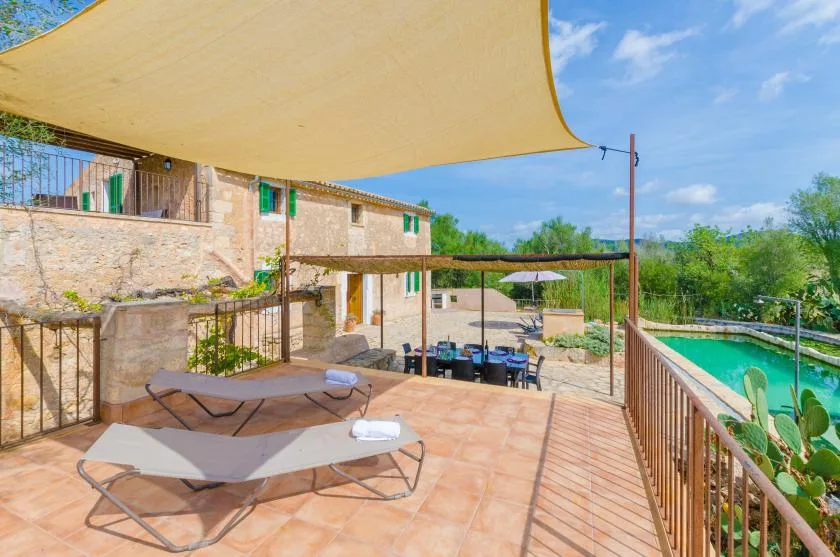 A shaded outdoor terrace overlooks a swimming pool beside a stone building.