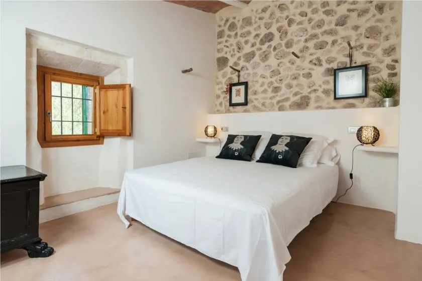 A bedroom with a white bed beneath a stone accent wall.