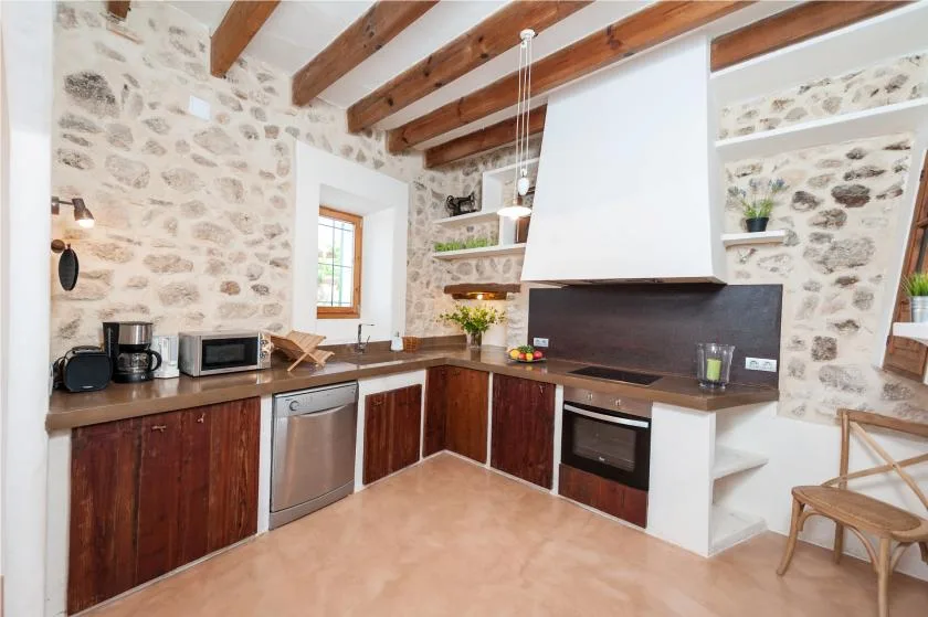 A rustic kitchen with stone walls, wooden cabinets, and a central cooking area.