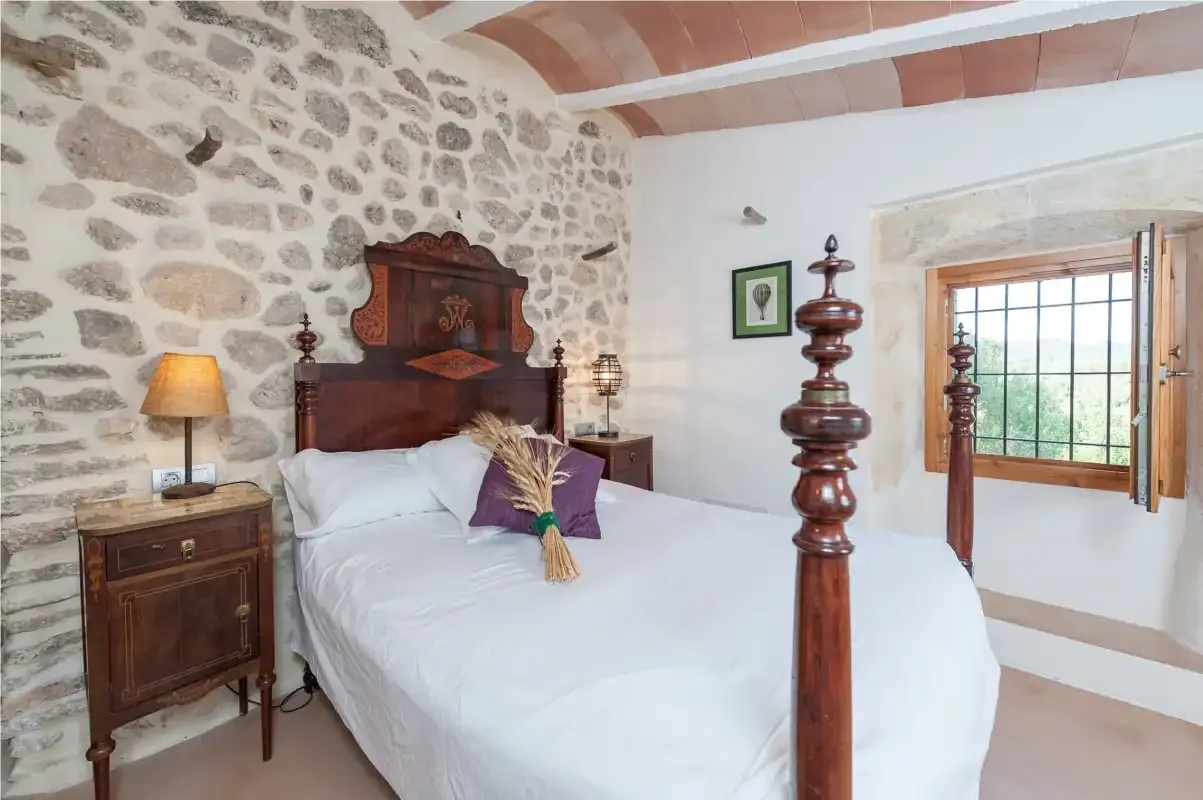 A bedroom with a white bed, stone wall, and wooden window.