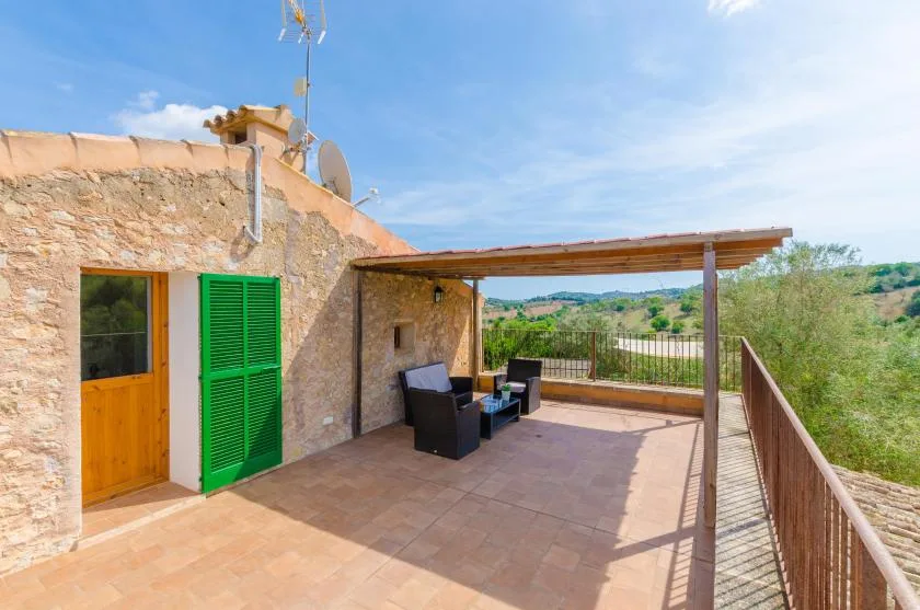A stone house opens onto a sunny terrace with shaded seating and countryside views.