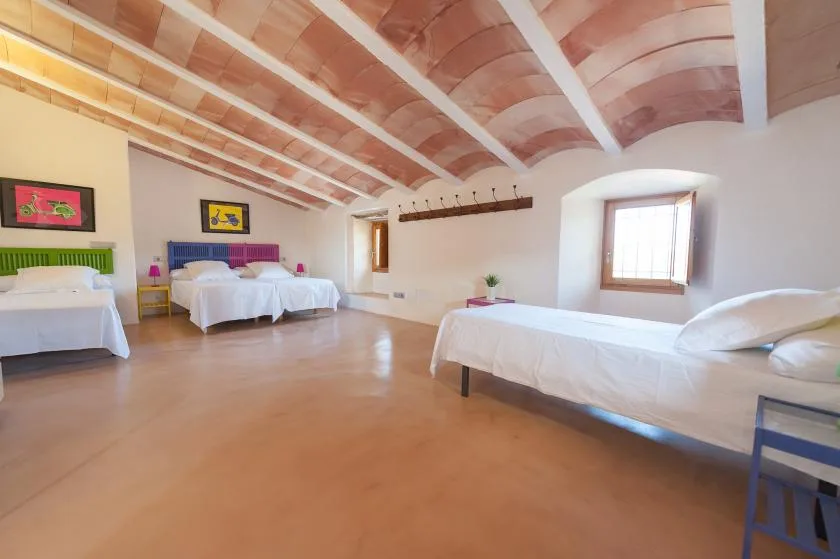 A bedroom with several beds beneath an exposed timber ceiling.