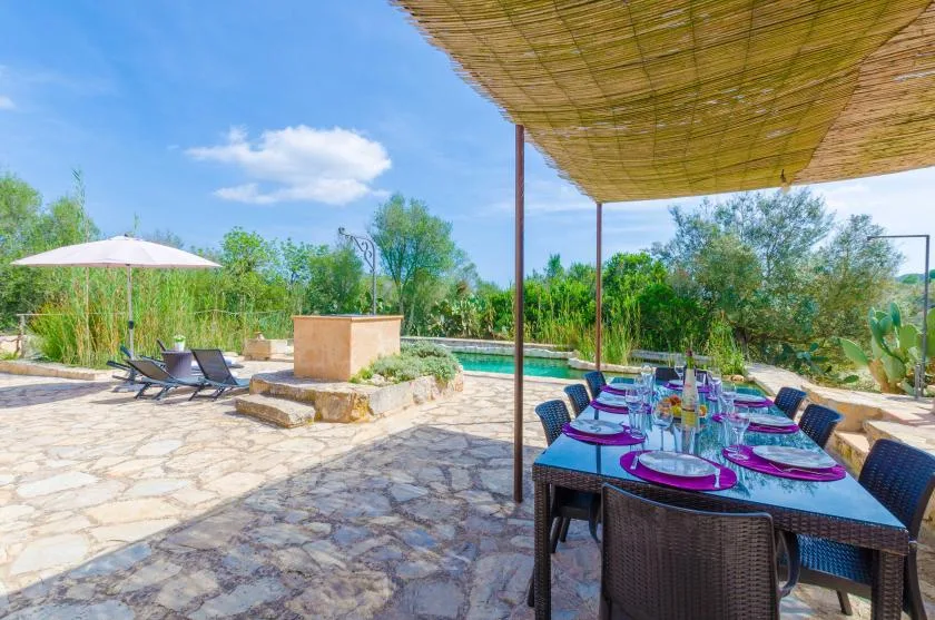 An outdoor dining area overlooks a swimming pool, with a shaded table set for a meal.