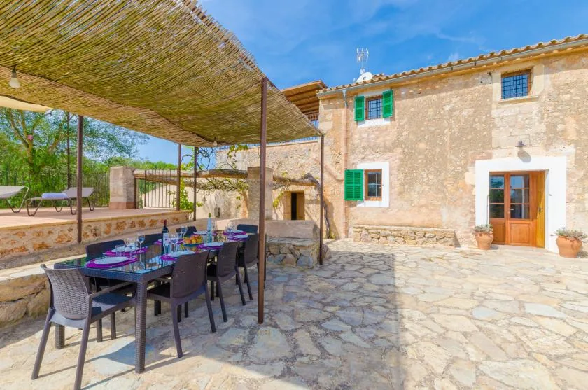 A stone patio with an outdoor dining table beneath a woven shade canopy.