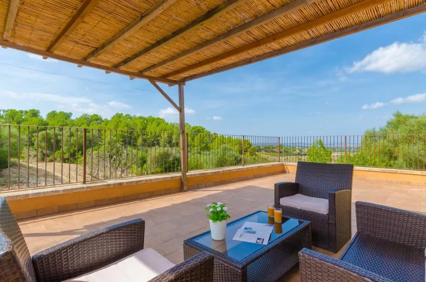 A covered outdoor terrace has seating around a low table overlooking greenery.