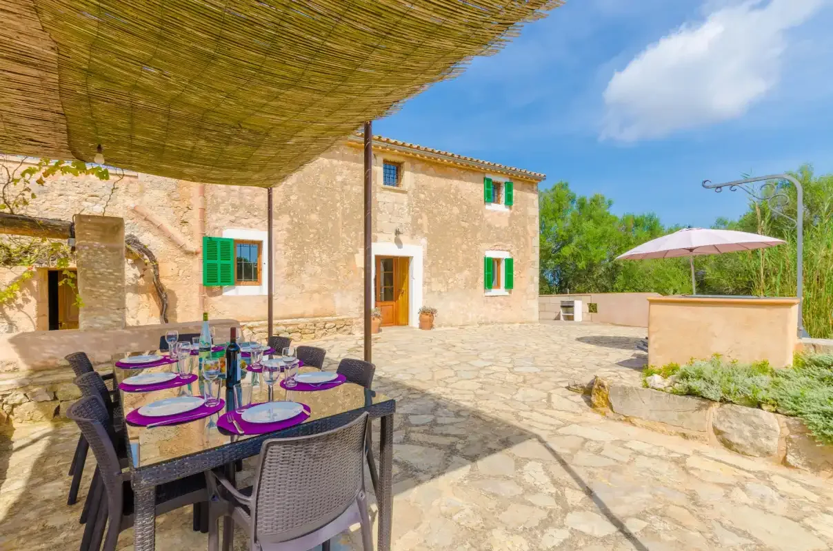 Stone house patio with outdoor dining seating and a sunshade.