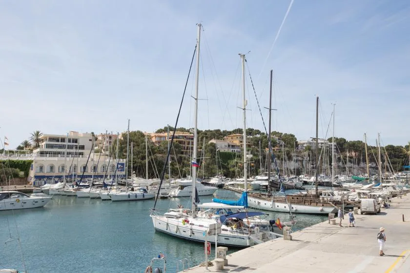 A marina with sailboats moored beside a waterfront promenade.