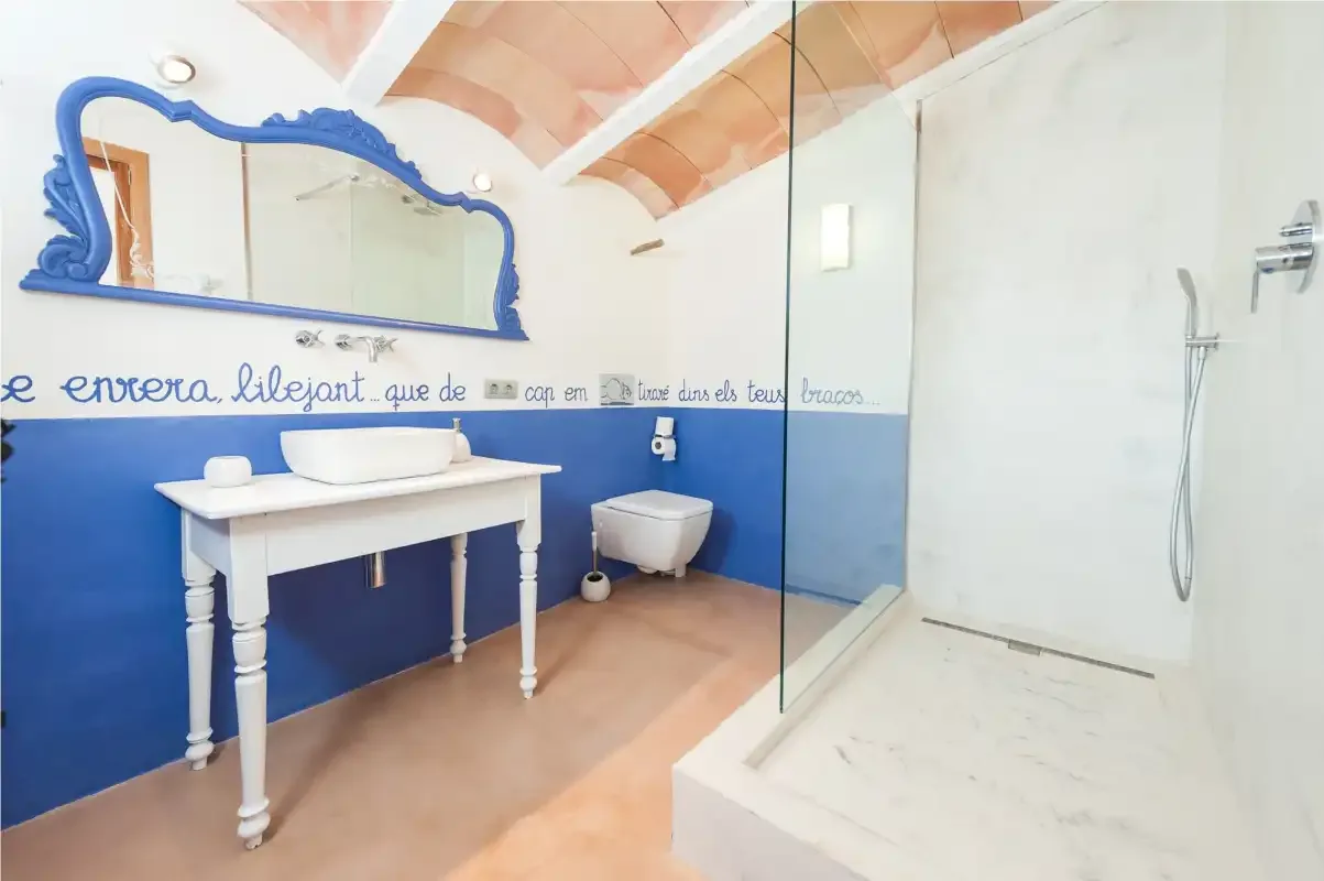 A bathroom with a white vanity, blue walls, and a glass shower screen.