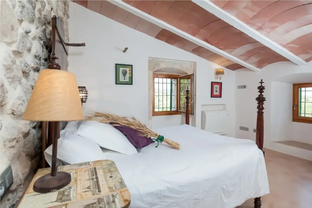 A bedroom with a large bed beneath a sloped ceiling and exposed beams.