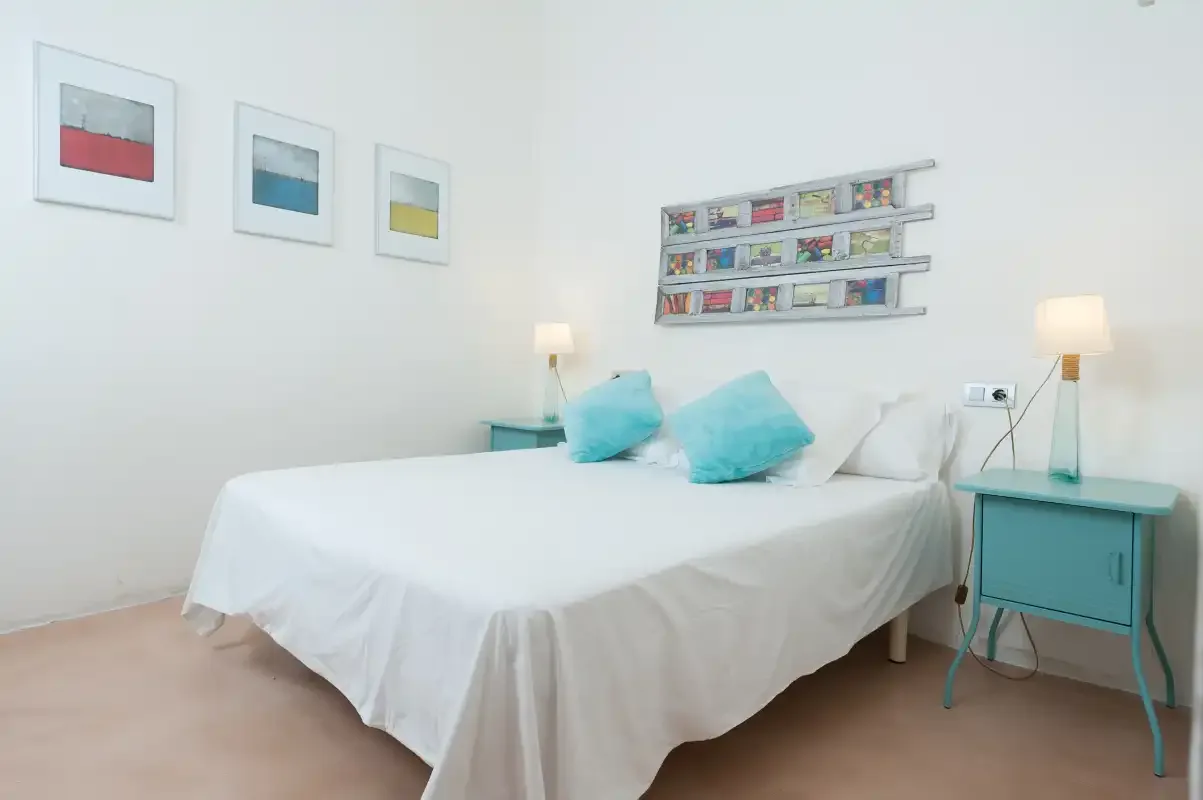 A bedroom with a white bed, turquoise pillows, and matching bedside tables.
