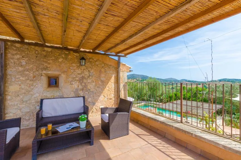 A covered outdoor seating area overlooks a pool and green hills.