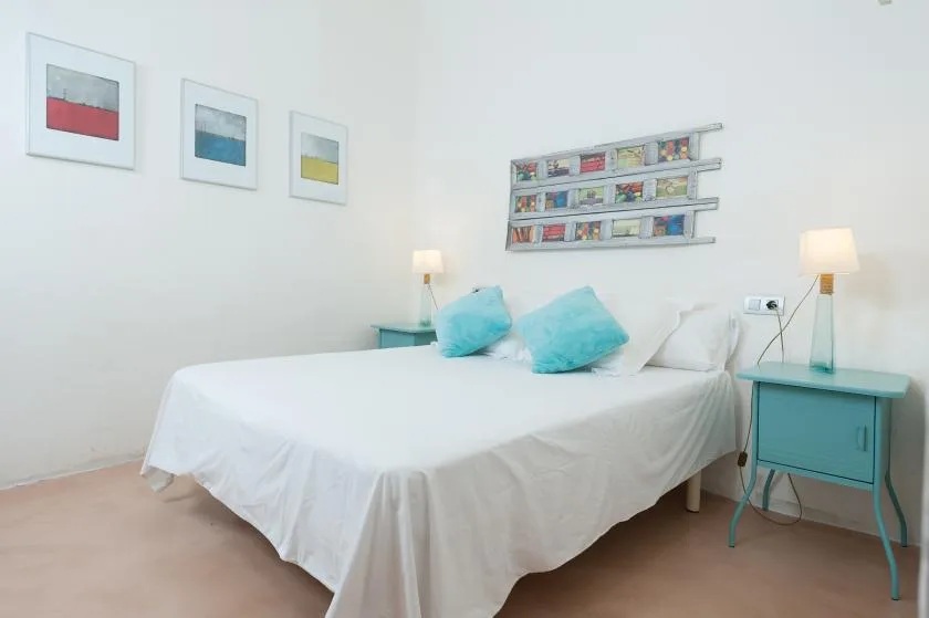 A bright bedroom with a white bed, turquoise pillows, and matching bedside tables.