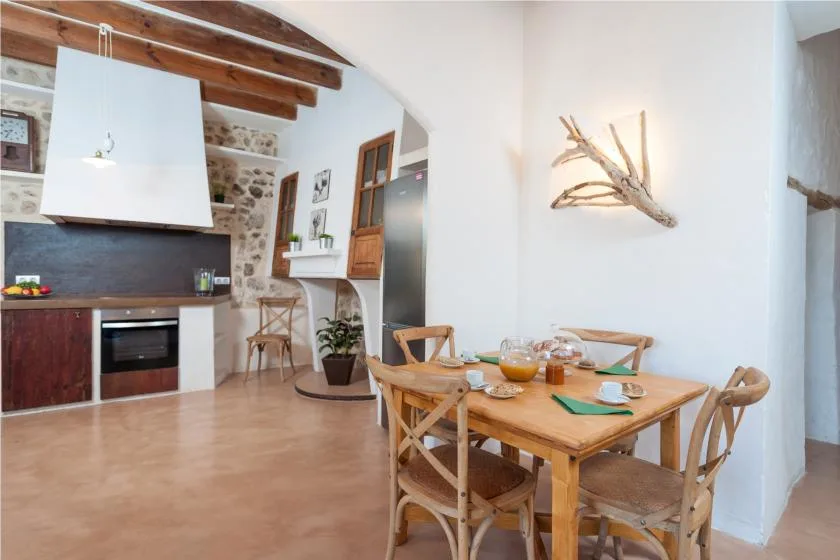 A dining area with a wooden table and an open kitchen behind it.