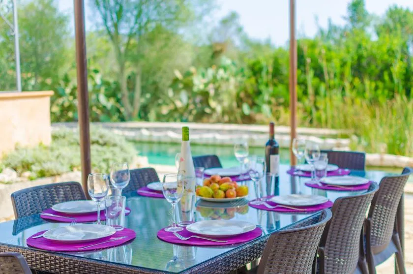 An outdoor dining table is set with plates and glasses beside a pool.