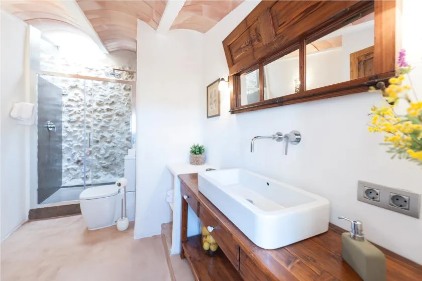 A bright bathroom with a white basin, wooden vanity, and glass shower.