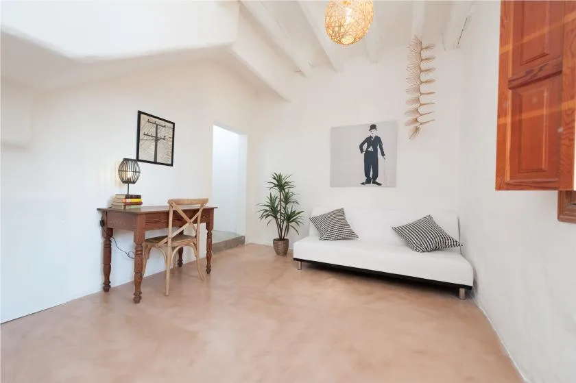 A bright sitting room has a low white bed and a small desk.