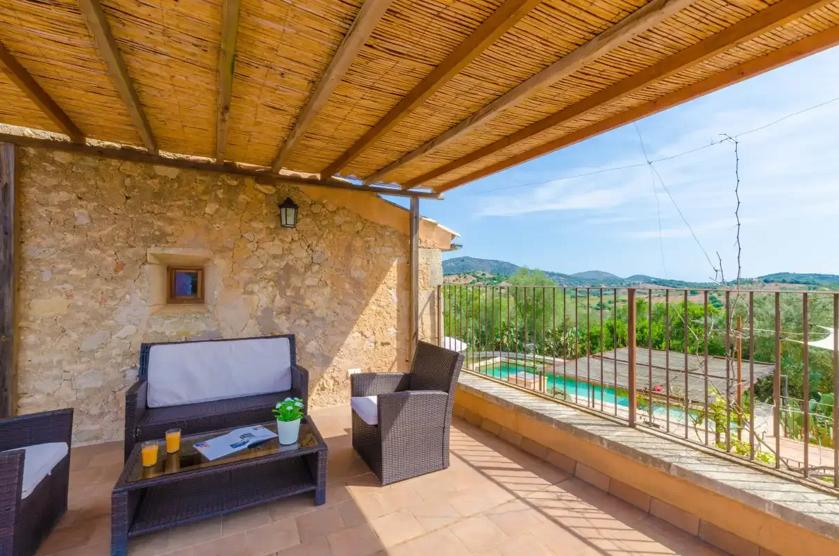 A covered outdoor terrace has seating beside a railing overlooking the landscape.