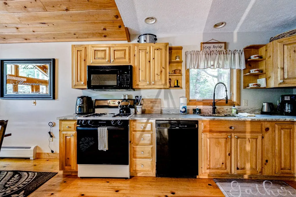 Una cocina con paneles de madera, estufa, microondas y fregadero bajo una ventana.