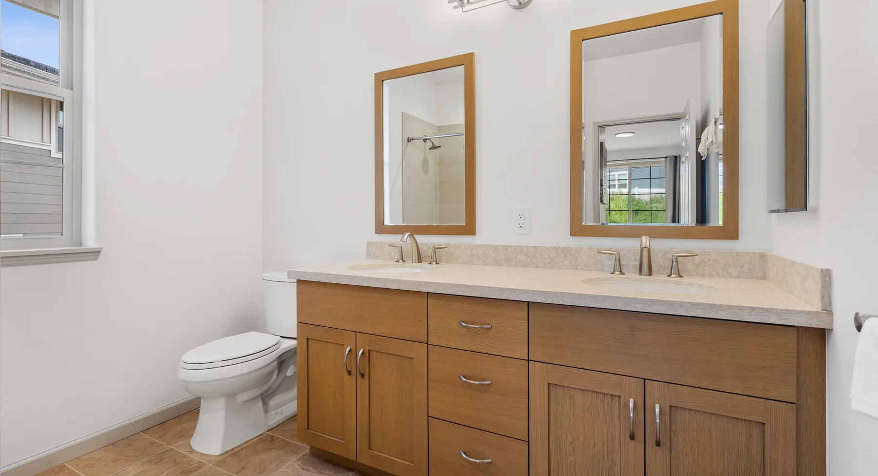Un baño luminoso con un mueble de madera, espejos y un inodoro.