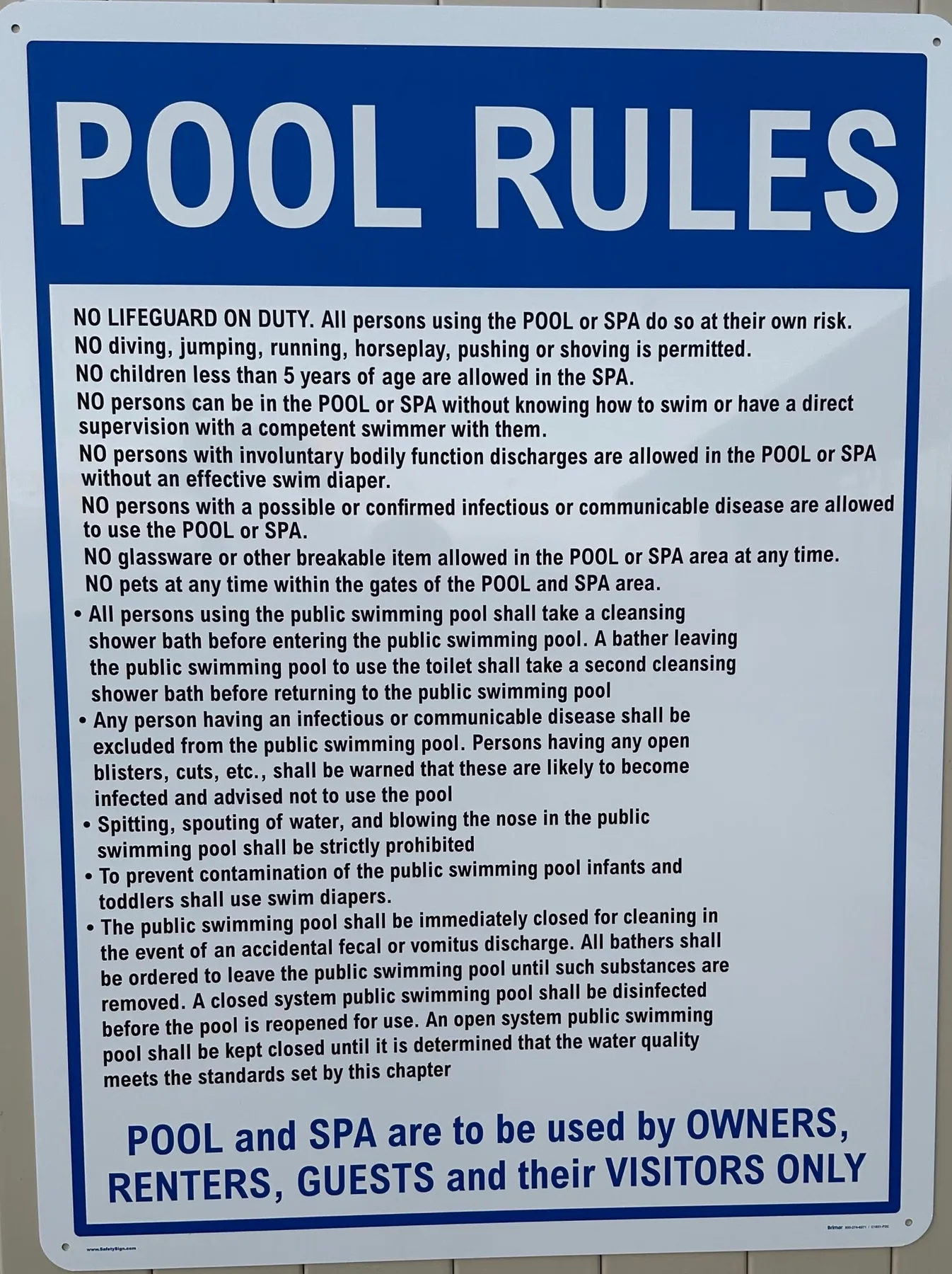 Un letrero azul con reglas de la piscina muestra instrucciones de seguridad en texto negro.