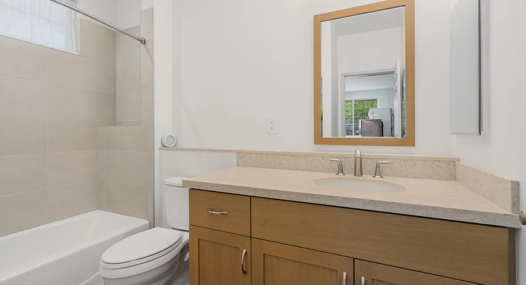 Un baño con bañera, inodoro y mueble de lavabo en tono madera.