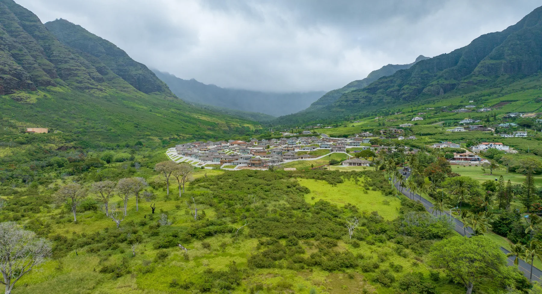 Un valle montañoso verde con un pequeño poblado bajo un cielo nublado.