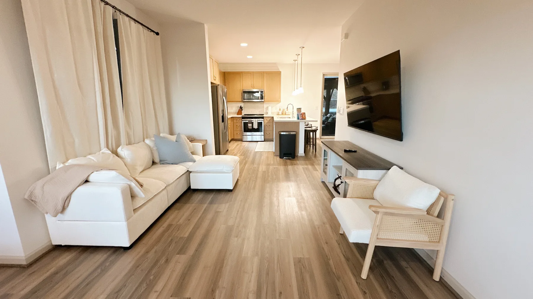 Una sala de estar se abre a una cocina, con asientos y un televisor en la pared.