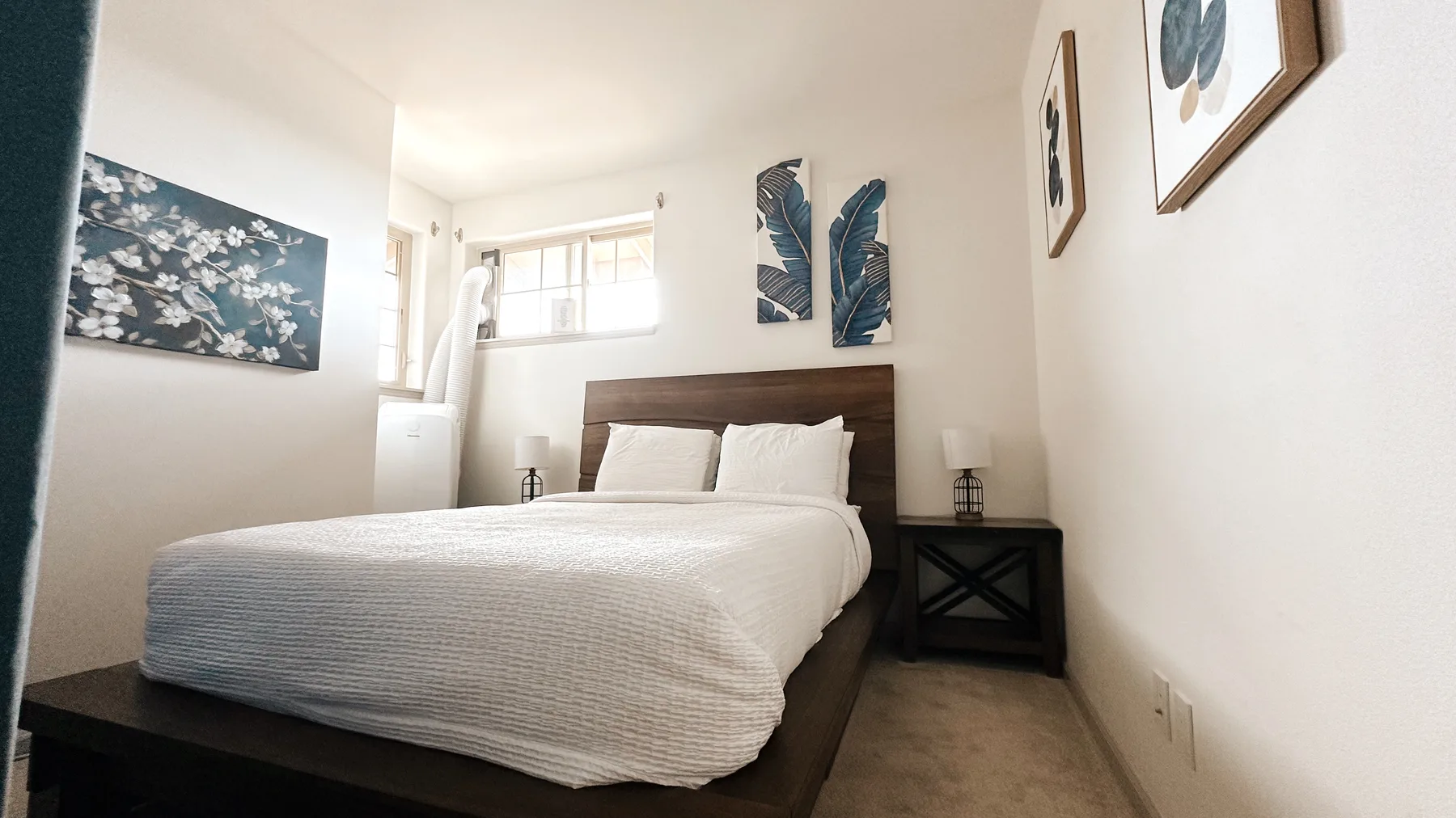 Un dormitorio luminoso con una cama bien tendida y láminas botánicas enmarcadas.
