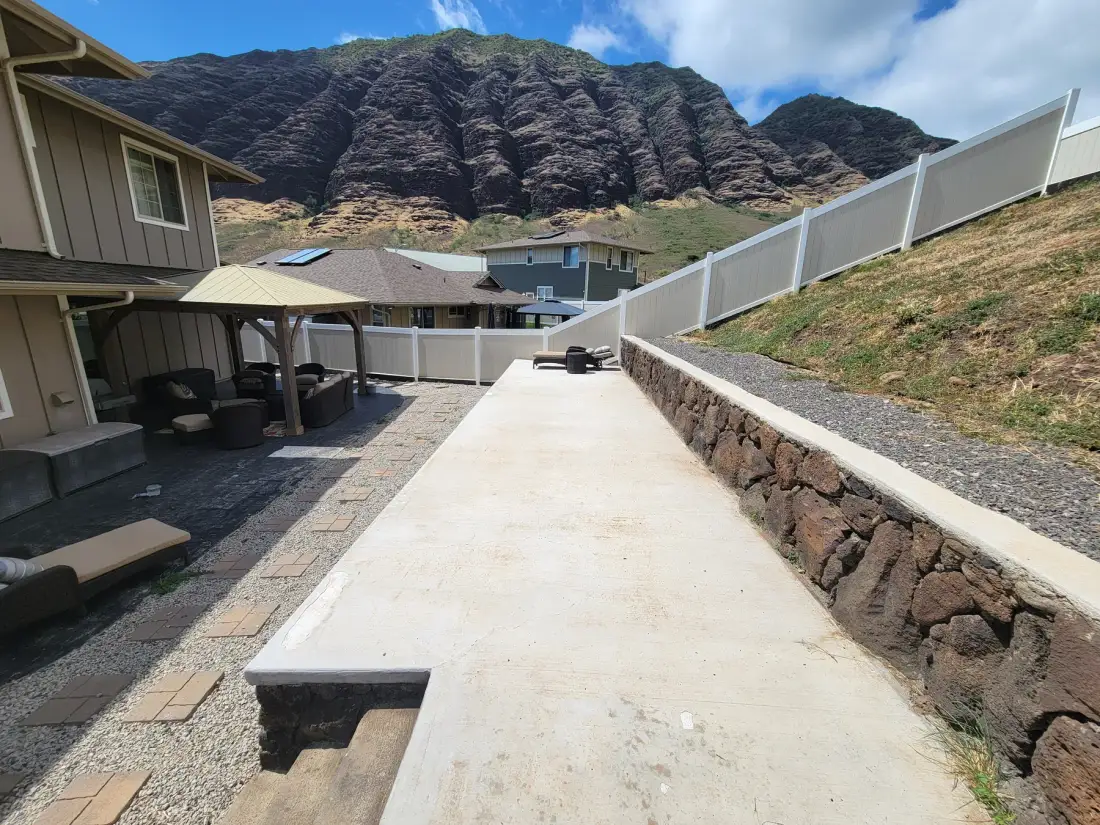 Un camino pavimentado al aire libre pasa entre un muro de contención de piedra y casas cercanas.