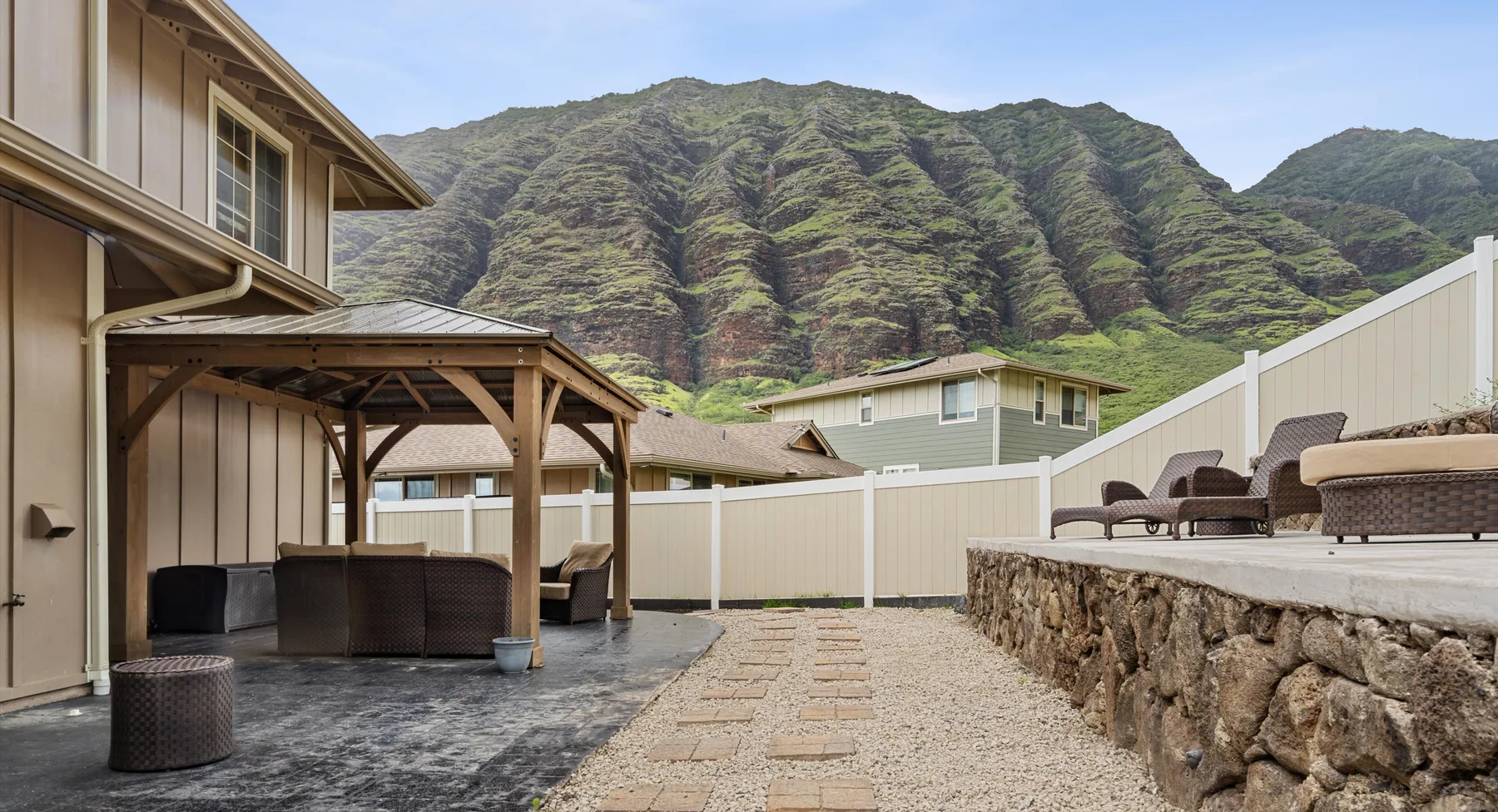 Un patio exterior con asientos cubiertos y un muro de piedra, con montañas verdes al fondo.