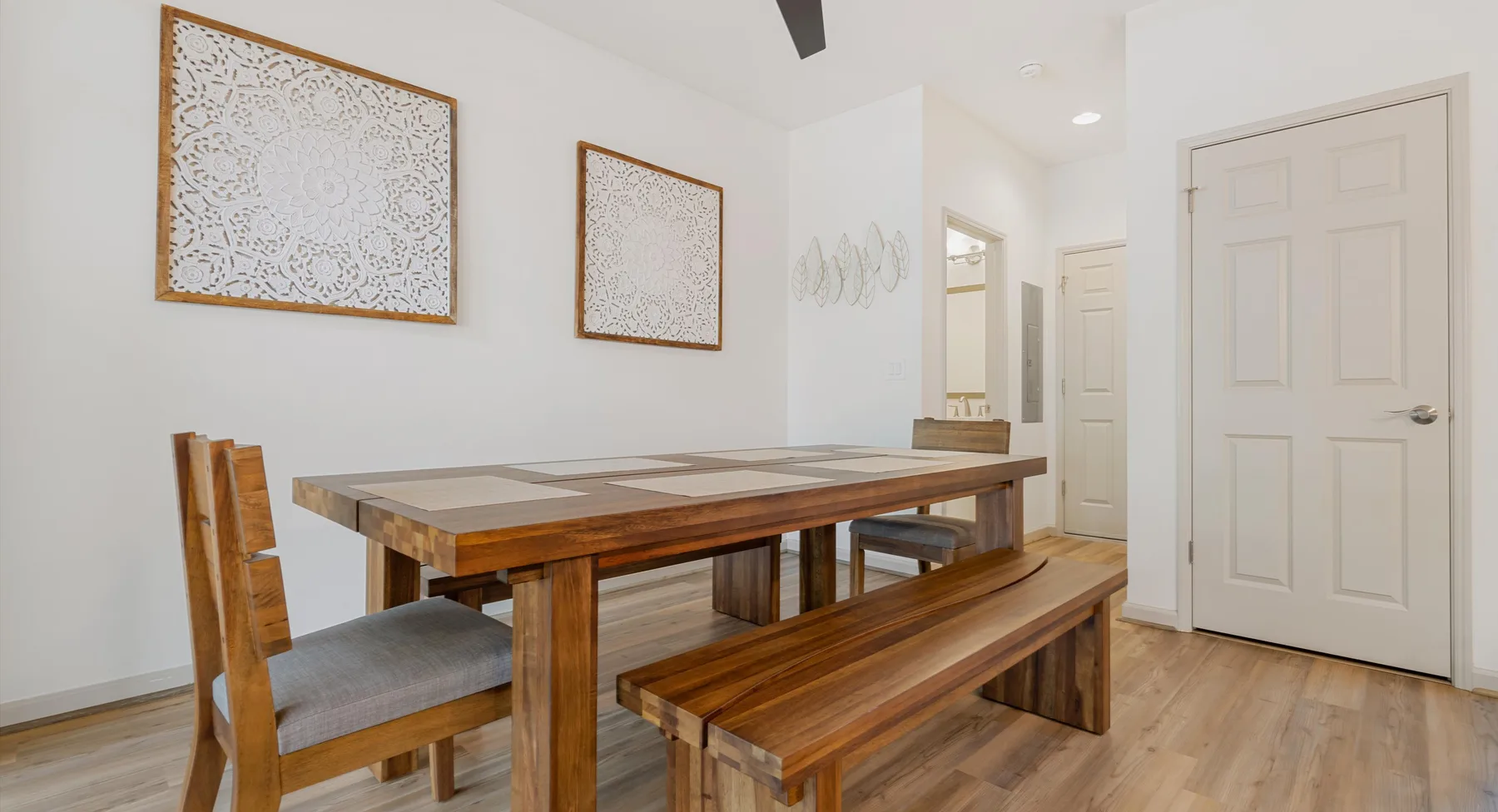 Un comedor luminoso con una larga mesa de madera y bancos bajo cuadros enmarcados.